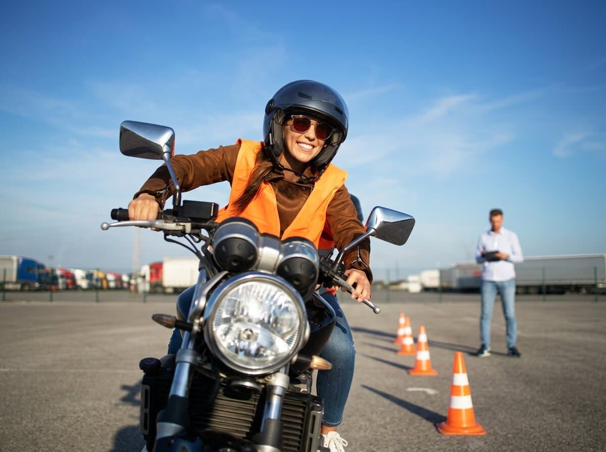 A learner in a helmet and safety vest practising on a two-wheeler at a training course